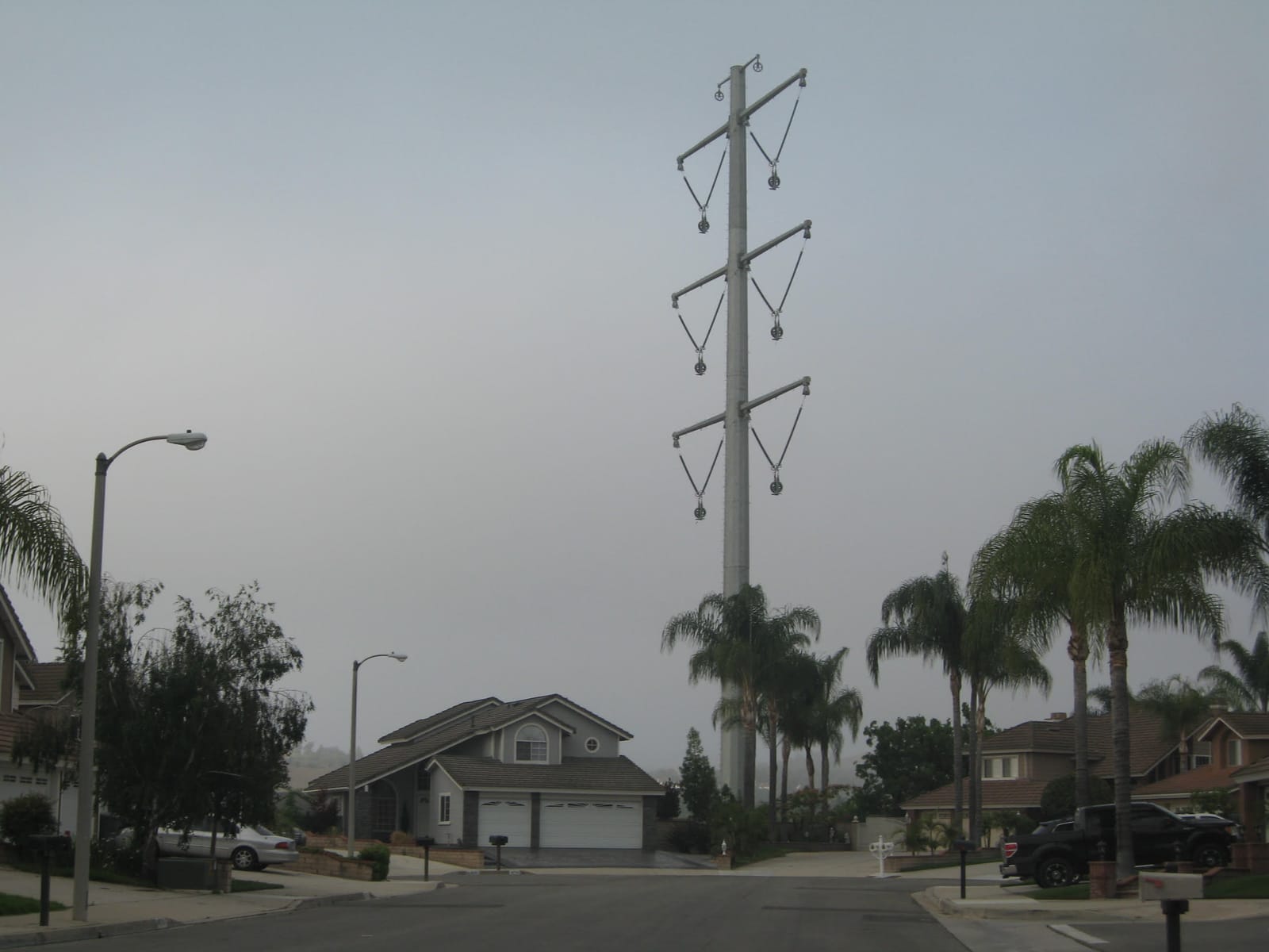 A nearly 200-foot tubular steel 500 kV transmission pole rising from a Chino Hills cul-de-sac, towering over two-story houses and palm trees.